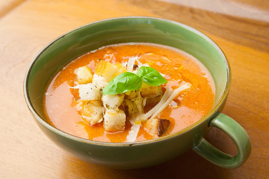 Tomato soup served in a soup cup with bread croutons, parmesan and basil