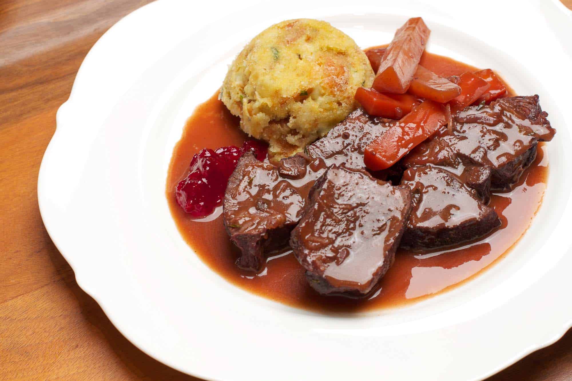 Roast venison recipe picture with dumplings as souffle, braised carrots, gravy and cranberries.