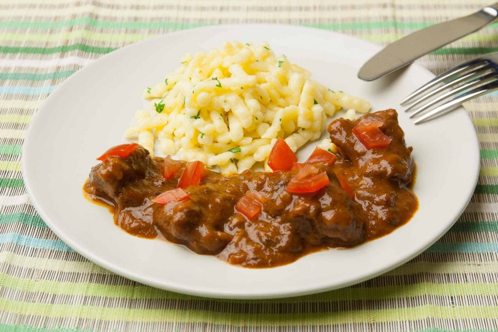 Beef goulash served with spaetzle, parsley and diced tomatoes