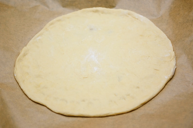 Yeast dough on the baking paper formed into a pizza.