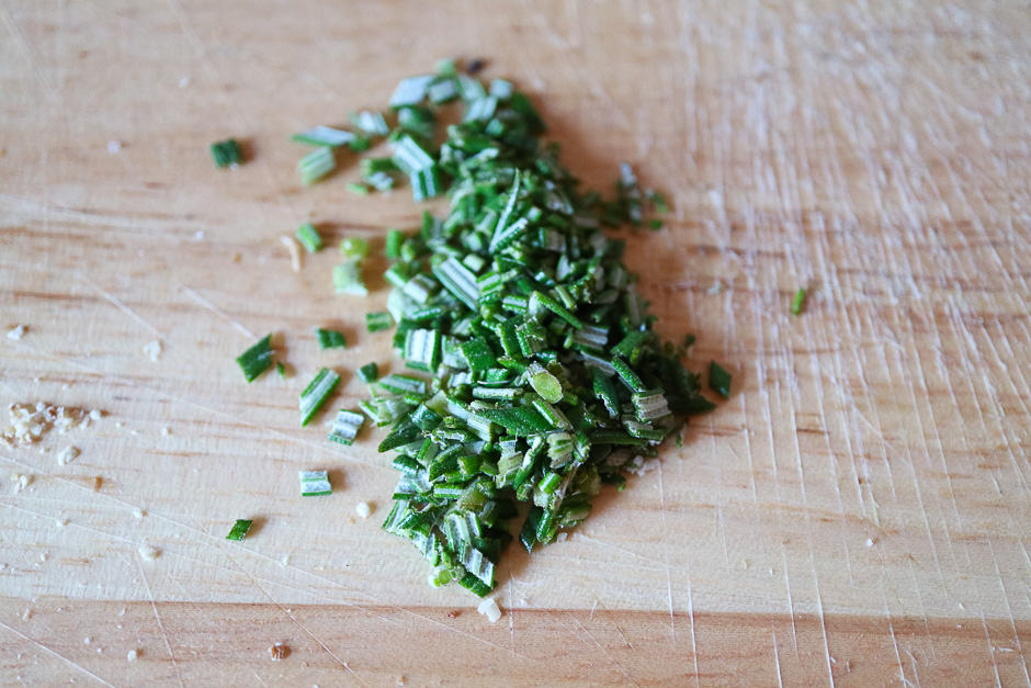 Rosemary needles finely chopped on a kitchen board.