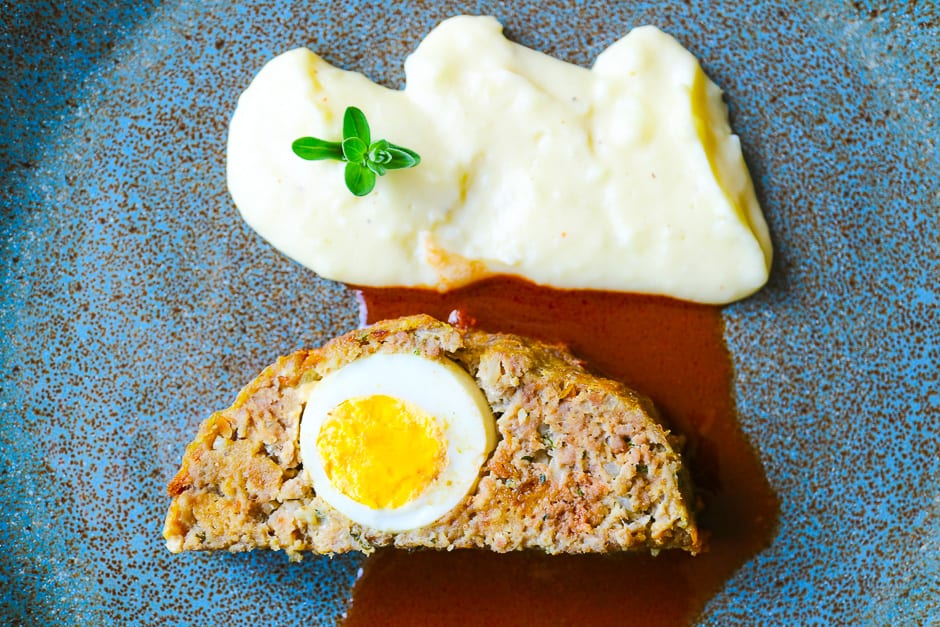 Meatloaf with egg, sauce and mashed potatoes on a blue plate.