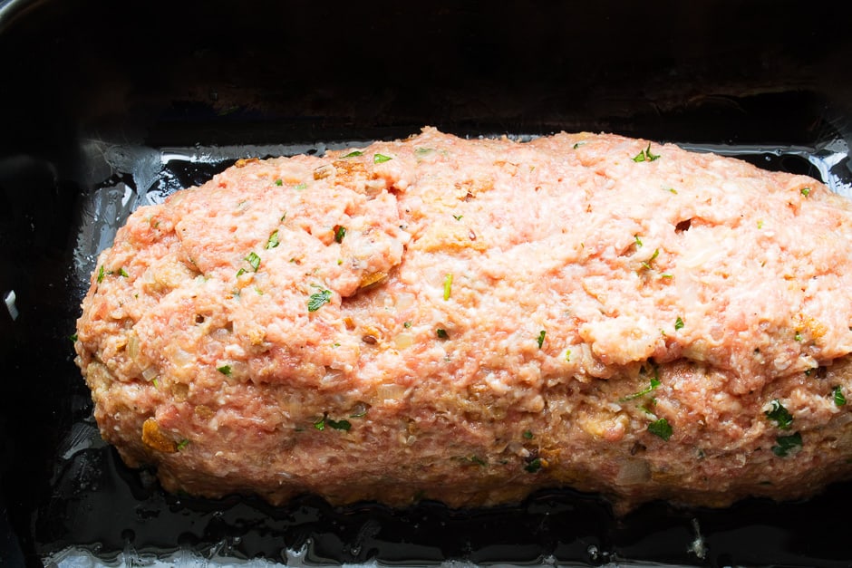 Shaped meatloaf, raw rabbit in a roasting pan.