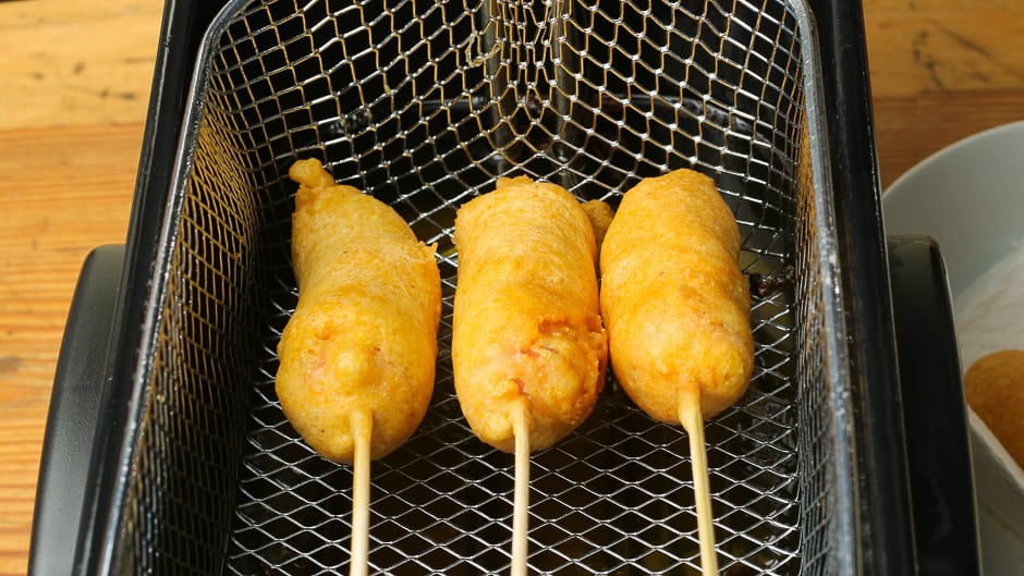 The corn dogs are ready. crispy fried sausages in corn batter in the basket of the deep fryer.