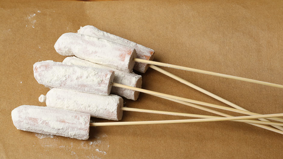 Sausages on wooden skewers coated with flour.