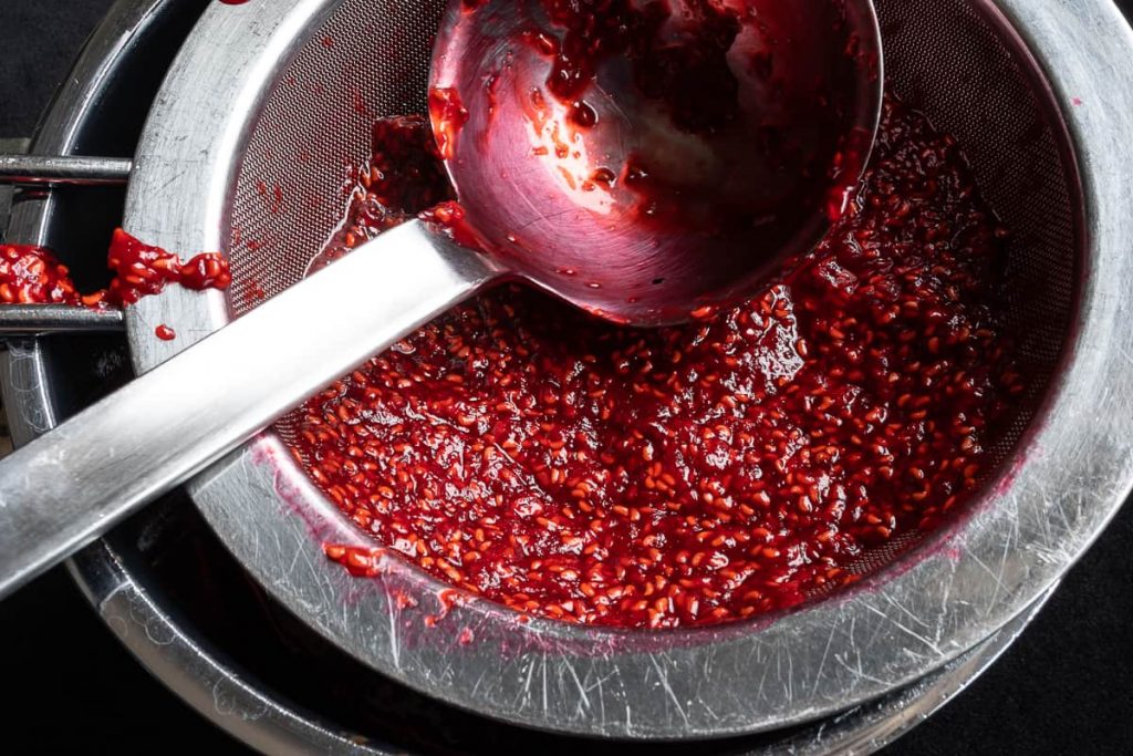 Strain raspberry jam through a sieve with a ladle