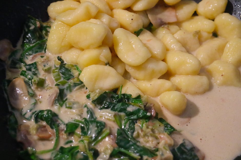 cooked gnocchi in a pan with spinach, mushrooms and cream sauce
