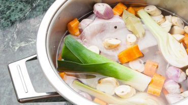 Fischfond mit Fischkarkassen und Gemüse im Topf.