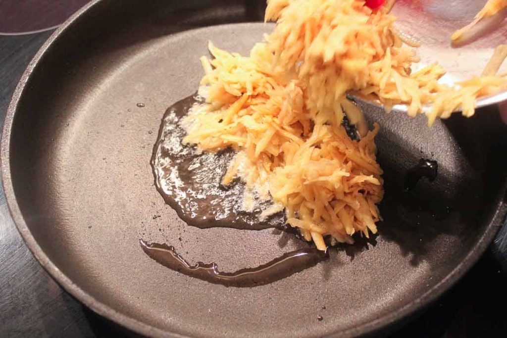 Geriebene, gewürzte Kartoffeln in die PFanne geben.