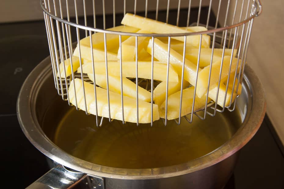 blanchierte pommes frites im frittierkorb über dem heißen Fett