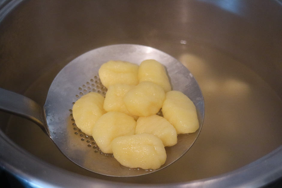 Frisch gekochte Gnocchi auf der Schaumkelle über dem Wasser.