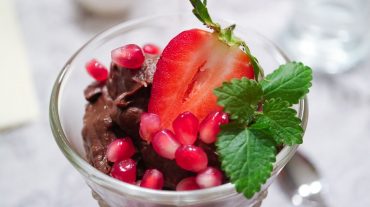 veganes Schokoladenmousse als dessert serviert, dekoriert mit Erdbeeren, Granatapfelkerne und Minze
