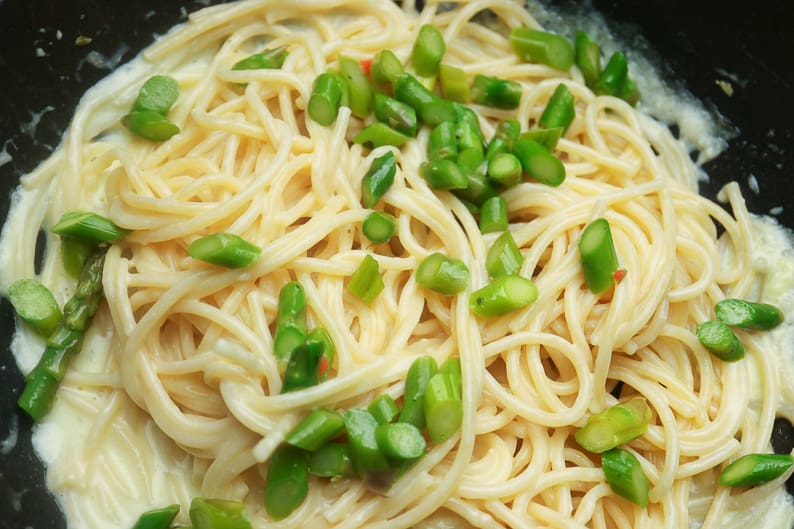Spaghetti mit Spargel und Soße in einer Pfanne beim vermischen.