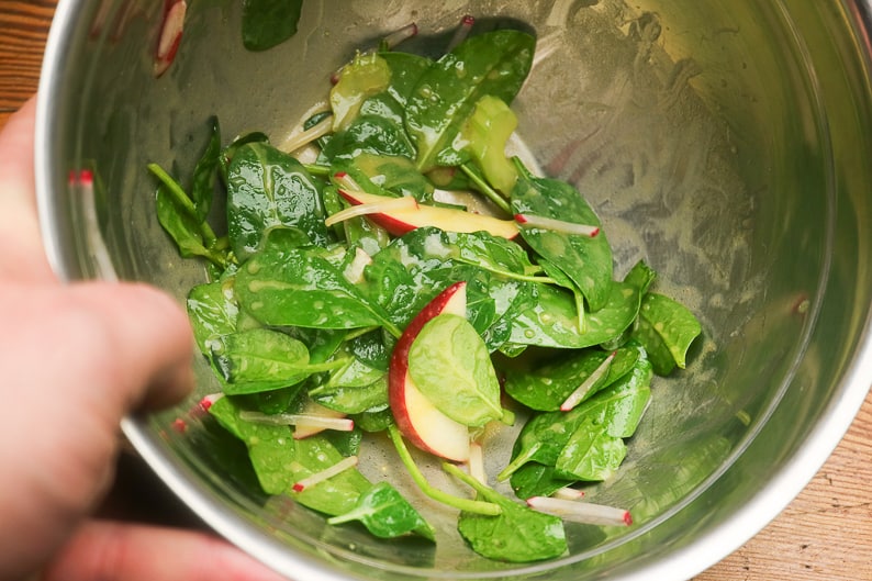 Salat marinieren: Spinatblätter, Apfelspalten, Radieschenjulienne und Sellerie in einer Schüssel mit Salatmarinade.