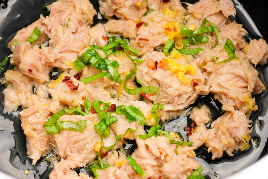 Thunfisch mit Öl, Basilikum, Zitronensaft und Zitronenabrieb sowie Chili in einer Pfanne.