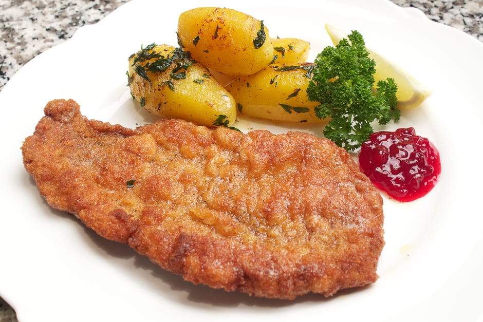 Wiener Schnitzel auf dem Teller angerichtet mit Prieiselbeeren und Petersilienkartoffeln.