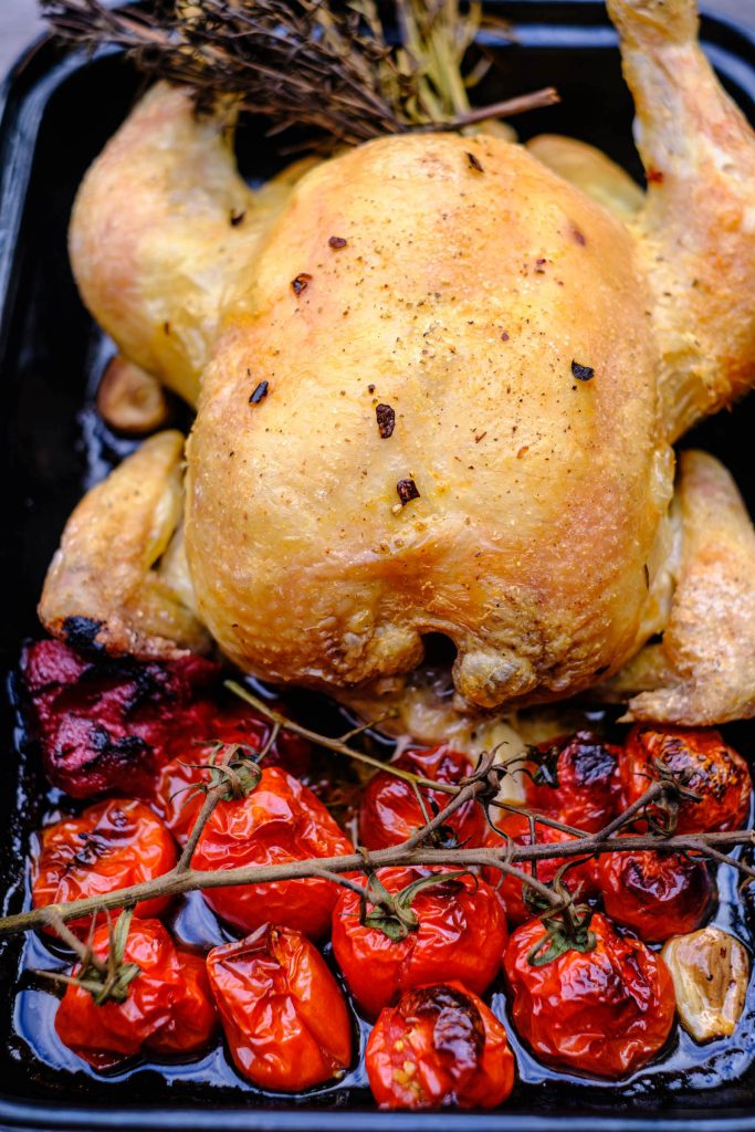 Gegartes Brathähnchen mit Tomaten im Bräter