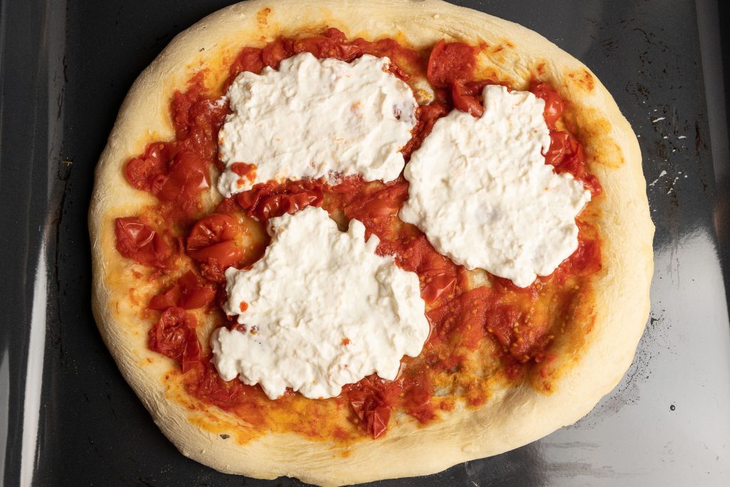 Pizza auf Backblech vorgebacken mit Käse ergänzt
