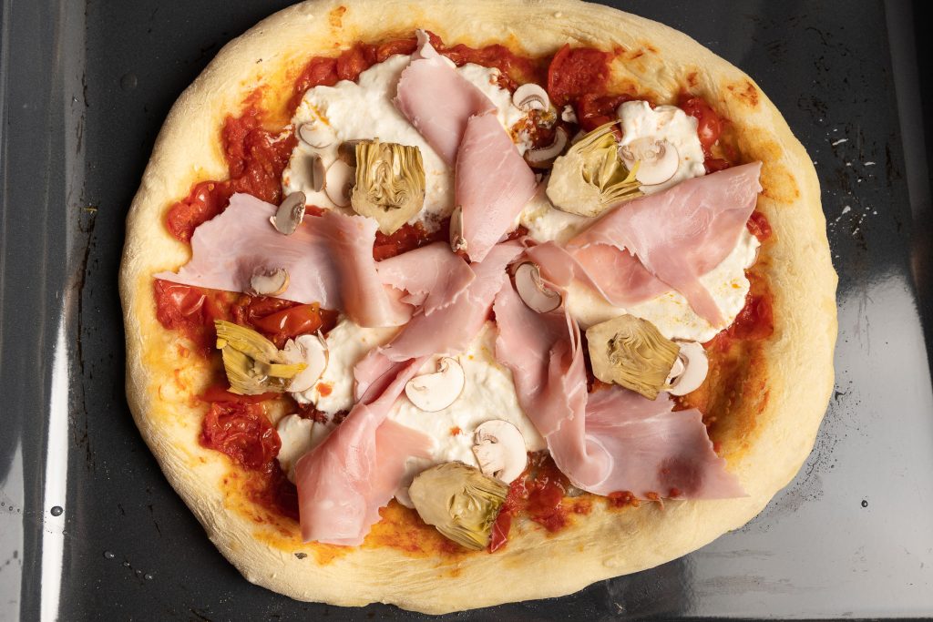 Pizza Capricciosa vorgebacken belegt mit Schinken, Artischocken und Champignons