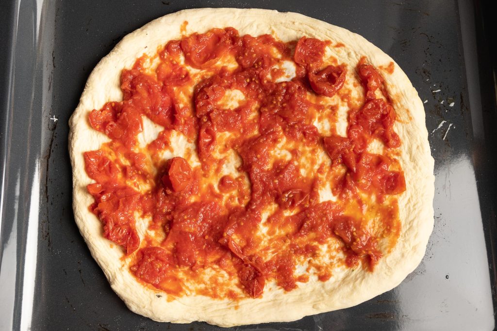Pizzateig ausgeformt auf dem Backblech mit Tomatensoße