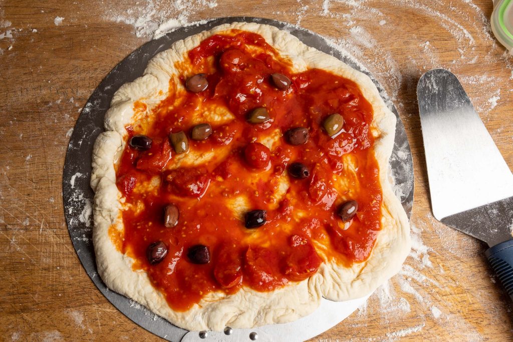 Pizzateig mit Tomaten und Oliven auf Pizzaschieber