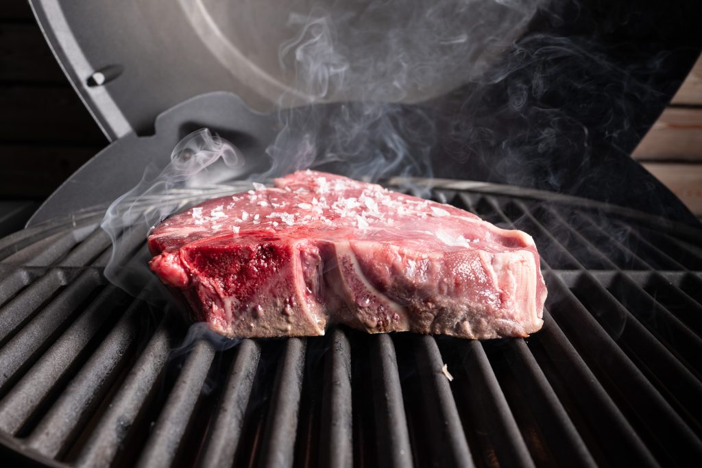 Porterhouse Steak auf dem Grillrost, seitlich fotografiert mit Rauch.