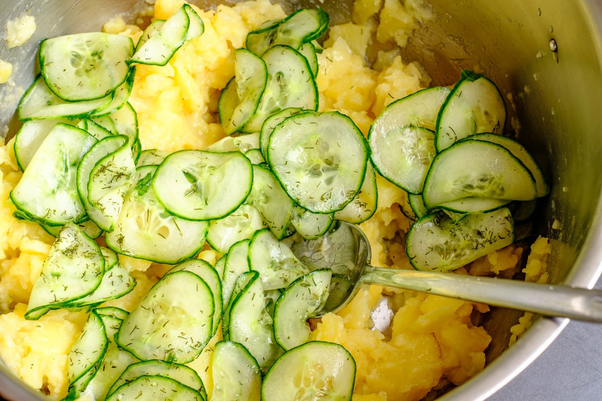 Salatgurken Scheiben zum Kartoffelsalat geben