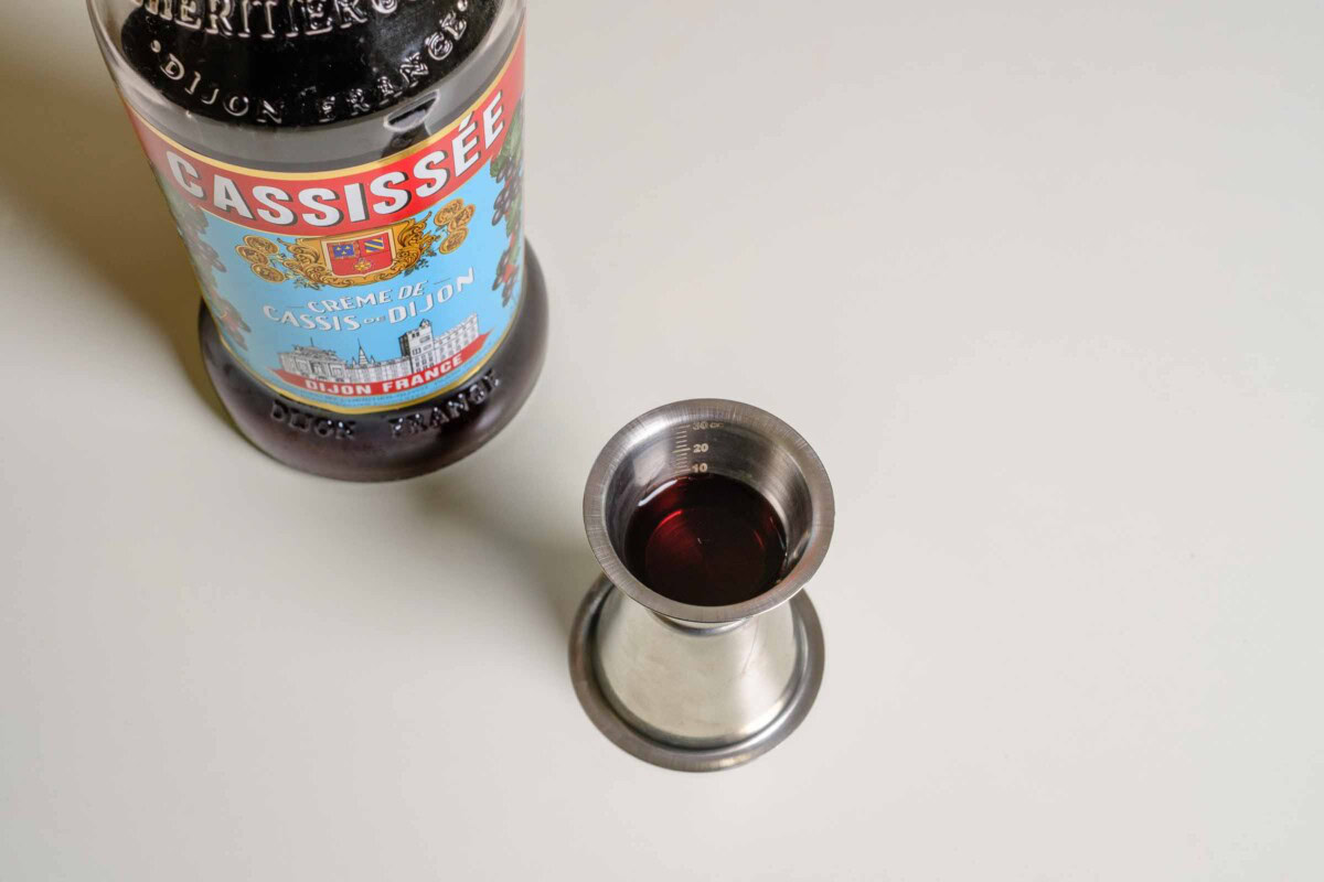 Cassis abmessen mit Jigger, Flasche im Hintergrund