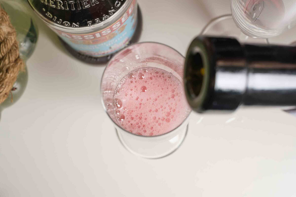 Champagner wird in ein Glas mit Cassis gegossen – klassische Zubereitung eines Kir Royal