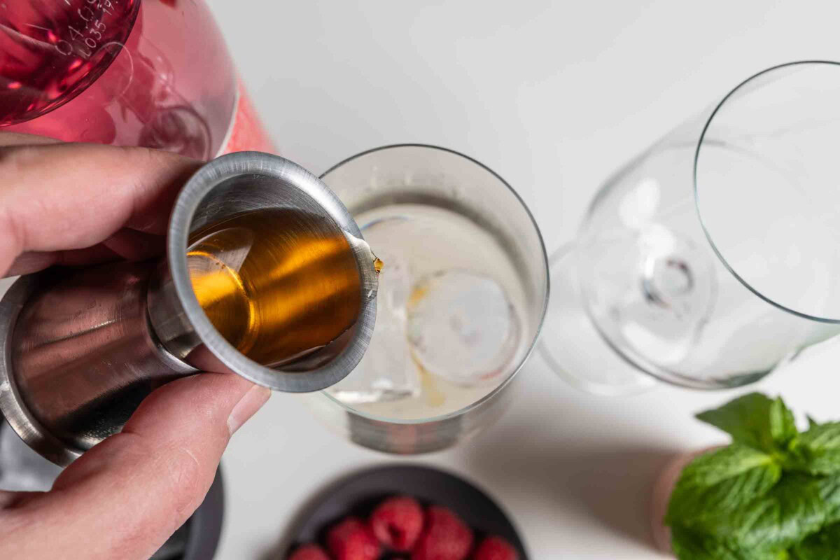 Cointreau wird mit einem Jigger ins Cocktailglas mit Eiswürfeln gegossen