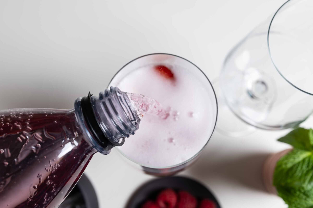 Schweppes Wild Berry wird in Cocktailglas mit Eis und Beeren gegossen