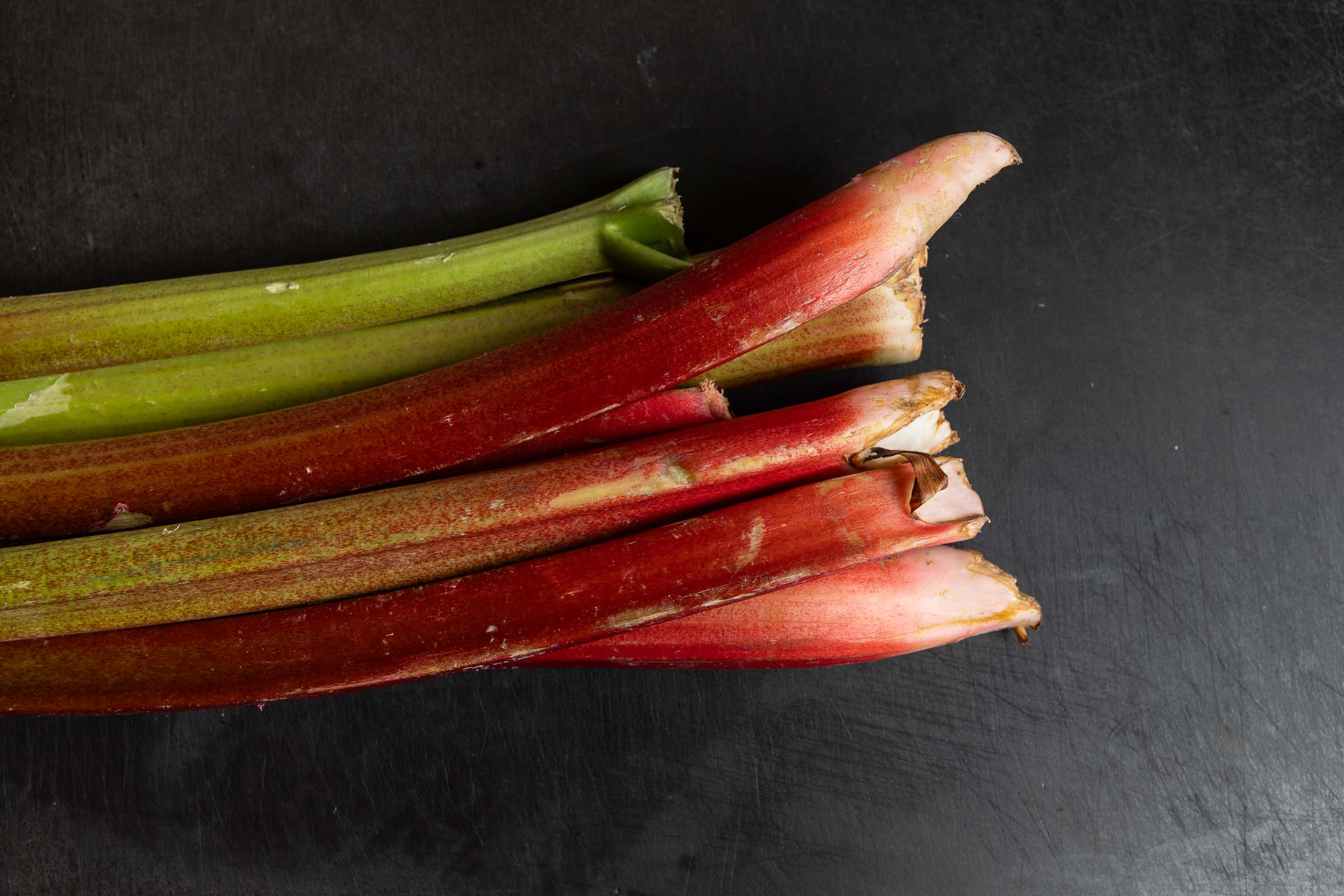 Frische, rote und grüne Rhabarberstangen auf dunklem Untergrund.