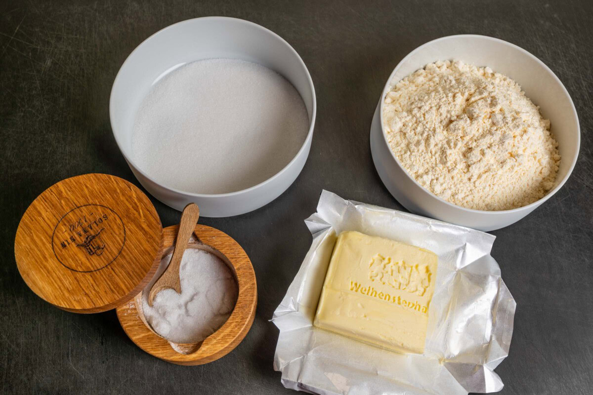 Zutaten für Mürbeteig: Butter, Zucker, Mehl und Salz auf schwarzem Untergrund. Das Ei Fehlt noch.