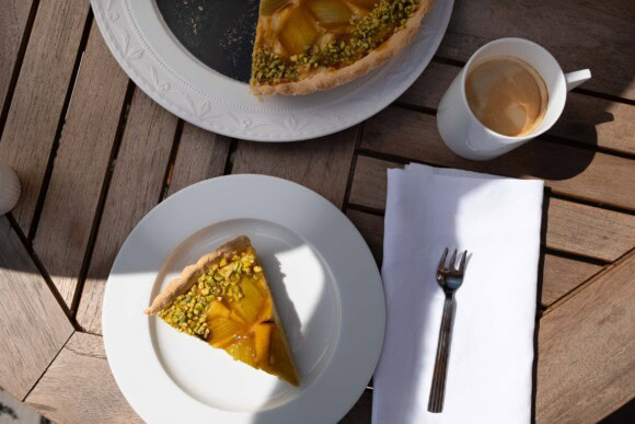 Rhabarber-Tarte-Stück mit Pistazien auf weißem Teller im Sonnenlicht